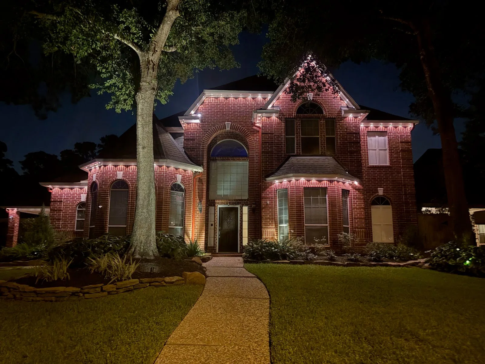 A real BrightSky two-story warm-white permanent roofline lighting installation on a Houston brick home