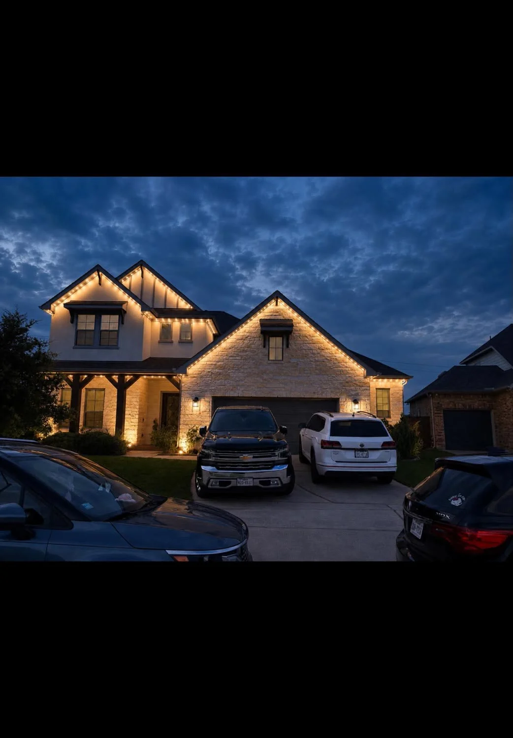 Real BrightSky install — warm-white permanent lighting outlining a two-story stone home at dusk